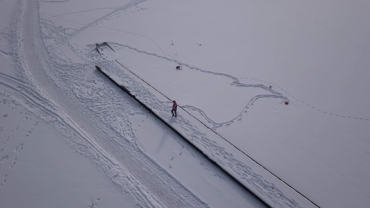 alejar imágenes aéreas que muestran a una mujer caminando sobre un embarcadero congelado hacia el final del muelle