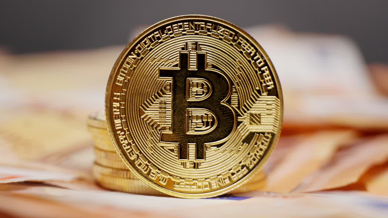 A gold Bitcoin coin stacked on top of other coins placed on a bed of euro bills