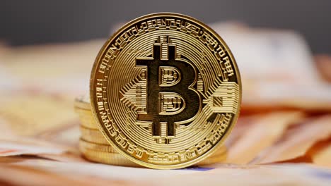 a gold bitcoin coin stacked on top of other coins placed on a bed of euro bills