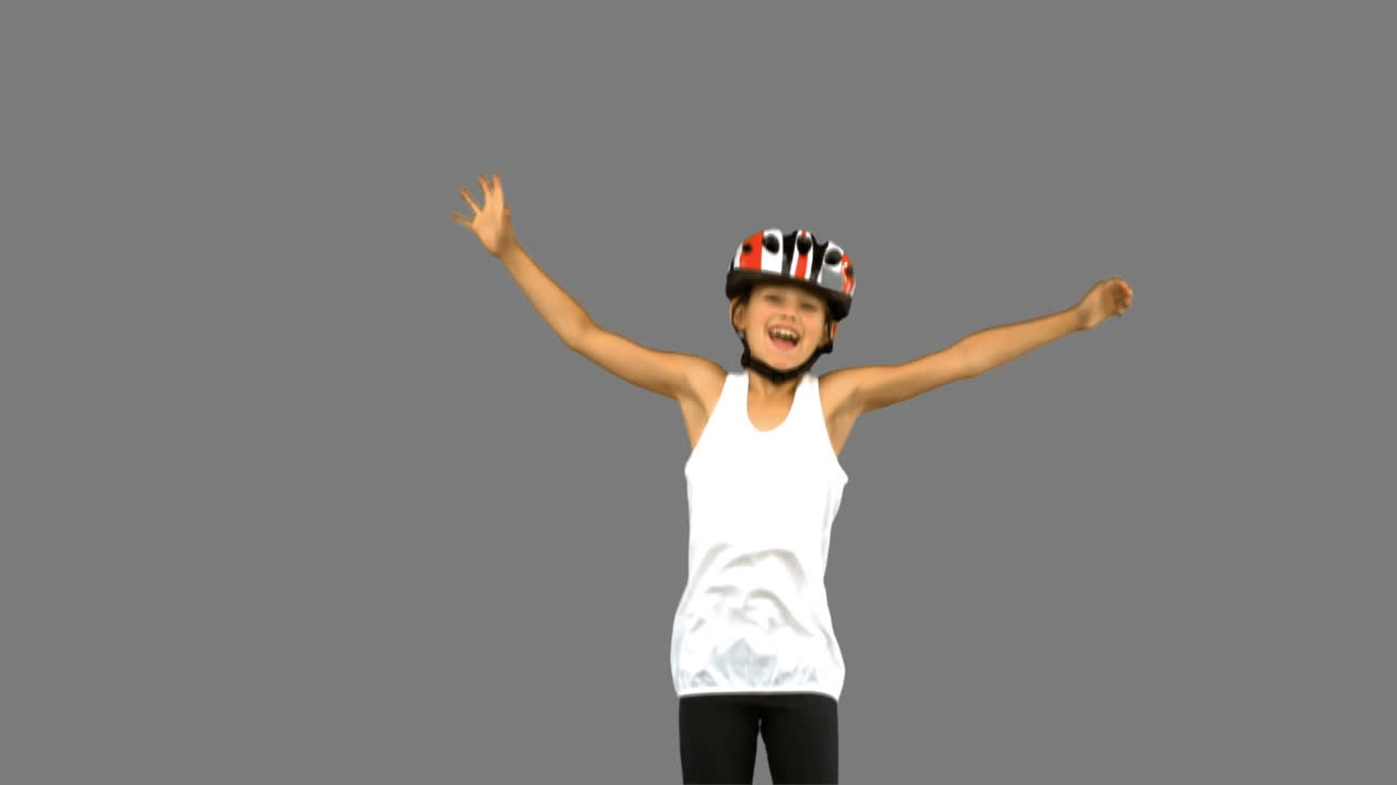 Ragazza carina che indossa un casco da bici e salta su schermo grigio