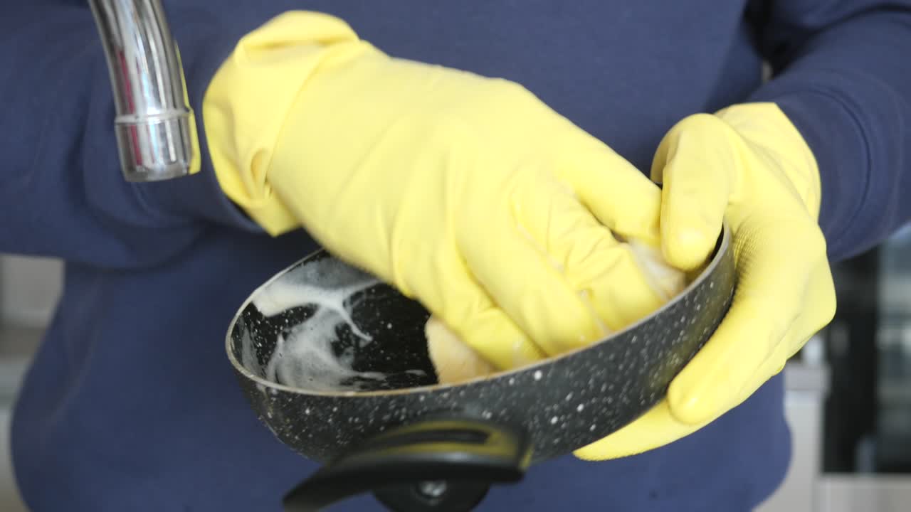 Hand mit Handschuhen spült einen Kochtopf