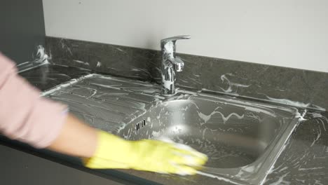 cleaning a kitchen sink with soap and gloves