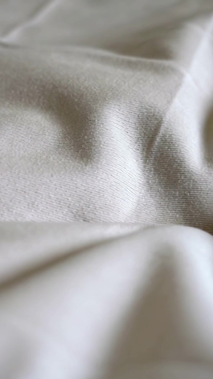 Vertical video: Shifting camera revealing closeup beige sheet on bed, showing ribbed weave and lint