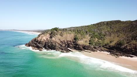 Aerial:-Drone-shot-rising-over-the-ocean-slowly-reveals-a-long-golden-sand-beach-beyond-the-headland,-south-of-Byron-Bay,-Australia