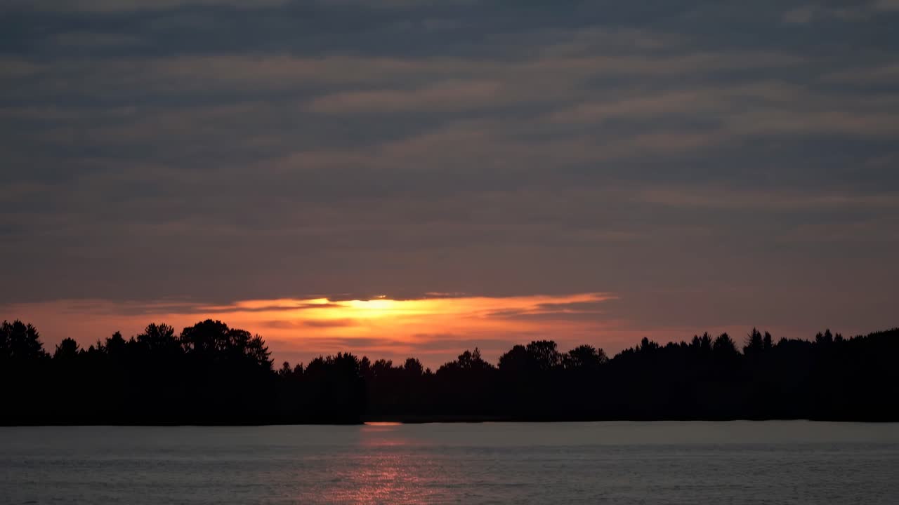 Serene sunset over a calm lake with silhouetted trees, captured from a low angle
