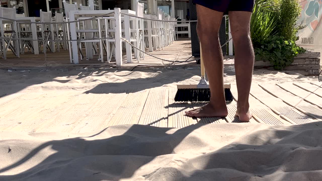 손에  ⁇ 자루를 들고 직원들은 캐파리카 해변으로 가는 나무로 된 보드워크에서 모래를 신중하게  ⁇ 아내며 해변 이용객들에게  ⁇ 끔하고 매력적인 경로를 보장합니다.