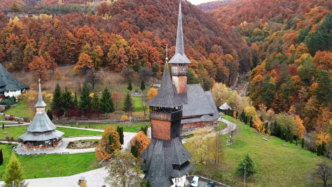 Aerial drone view of the Barsana Monastery, Romania. Main church and other buildings, visitors, hills covered with yellowing forest around