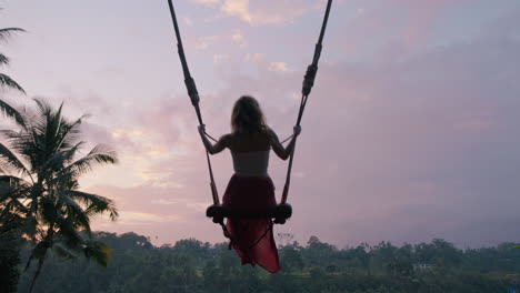 happy woman swinging over tropical jungle at sunrise travel girl enjoying exotic vacation sitting on swing in having fun holiday lifestyle freedom 4k