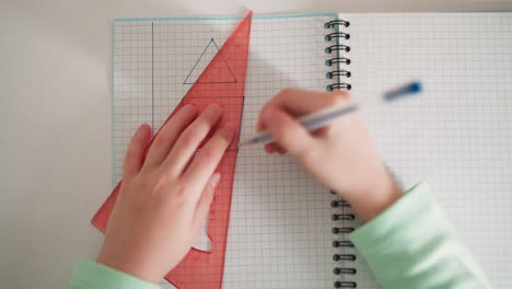 little student draws geometrical shape on exercise book page