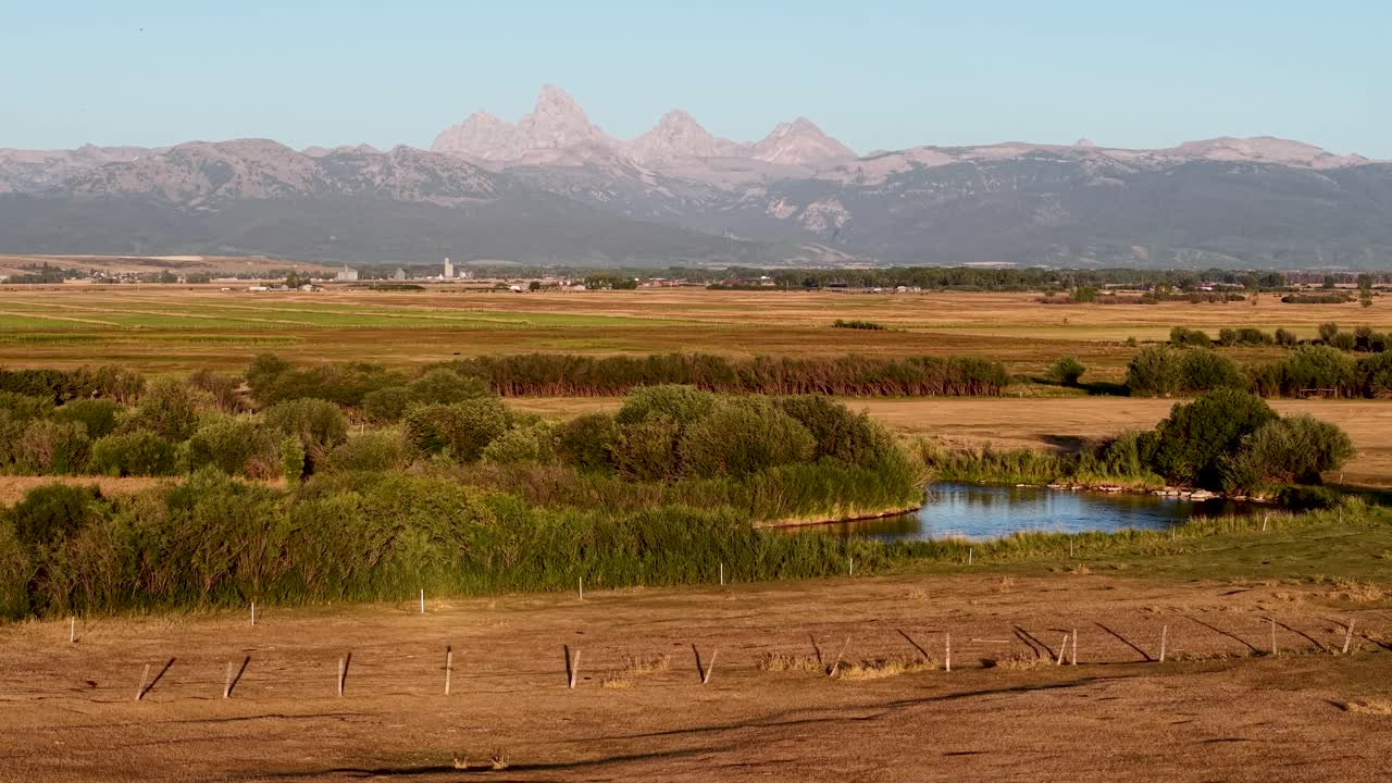 Vista aerea di terreni agricoli con canali di irrigazione e campi erbosi, piccoli stagni che riflettono il cielo e le cime delle montagne Teton sullo sfondo