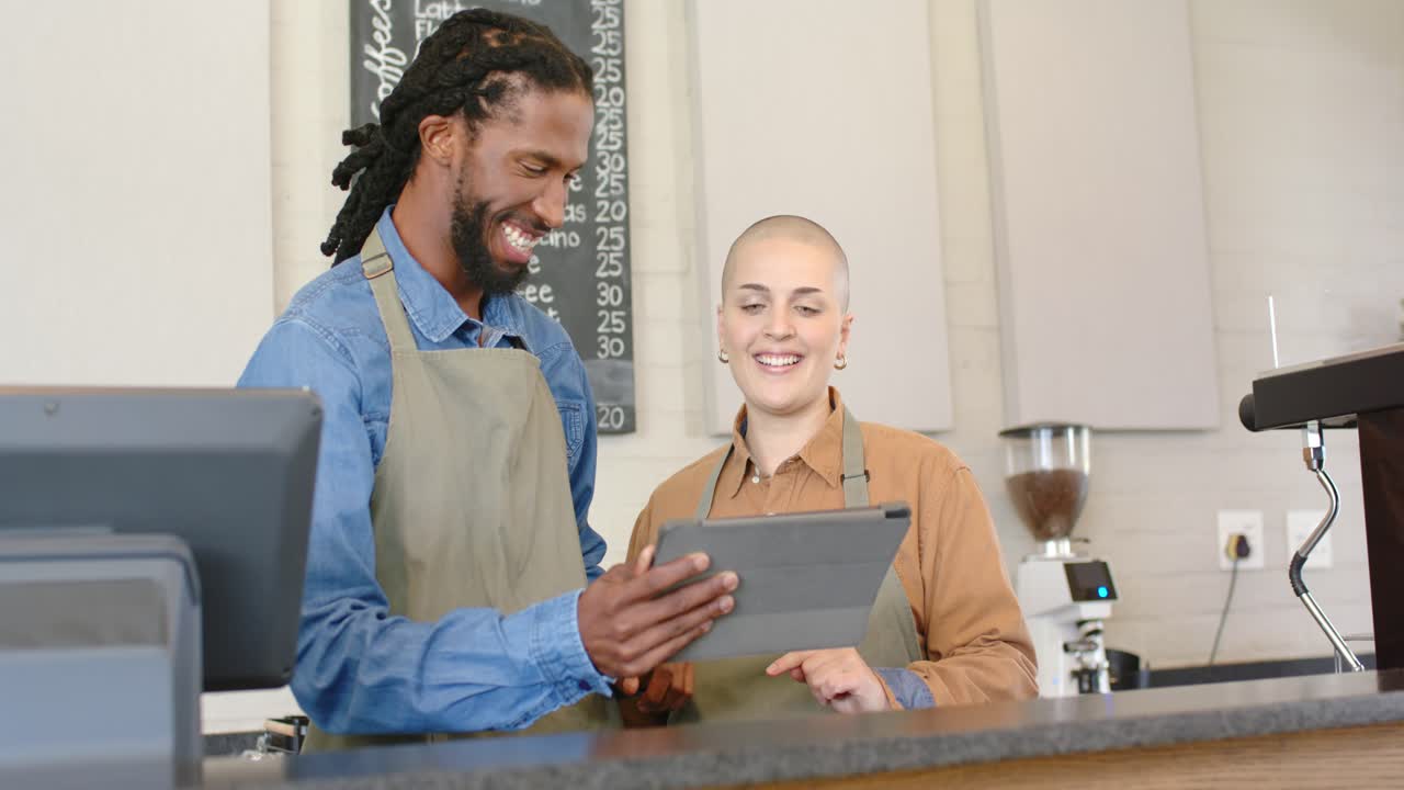 Diverse coworkers tapping tablet, reviewing information under chalkboard menu behind coffee machine