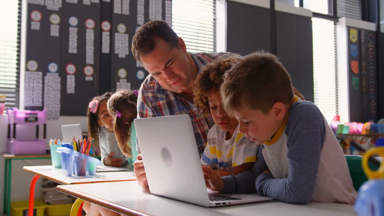 vista lateral del maestro caucásico que enseña a los escolares en la computadora portátil en el aula 4k