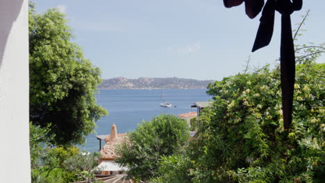 Serene-Sardinian-seascape,-lush-greenery,-sailboat-on-calm-waters