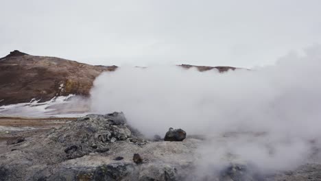 active rocky icelandic steam vent push out white vapor near orange mountain