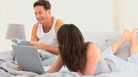 una mujer bonita en su portátil mientras su marido está leyendo