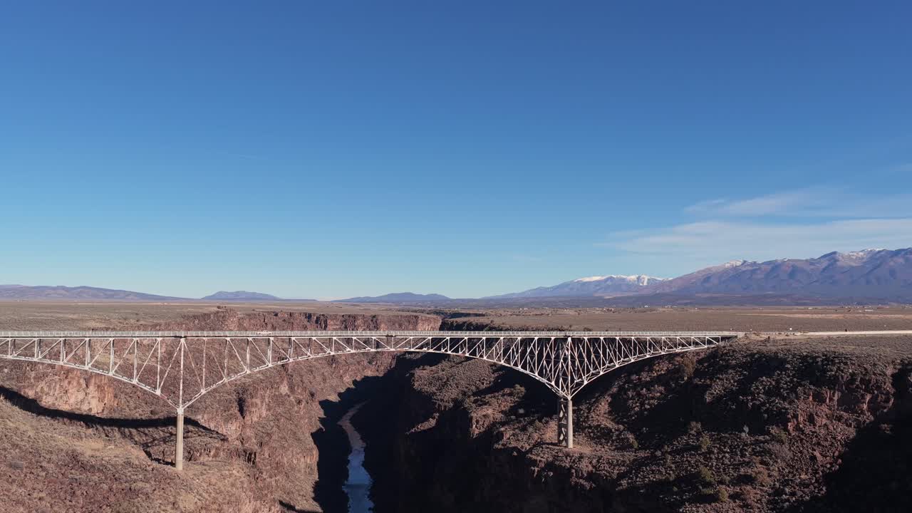 The view follows a single pickup truck as it crosses the massive span over the river canyon. This iconic Southwestern infrastructure is located near Taos, New Mexico