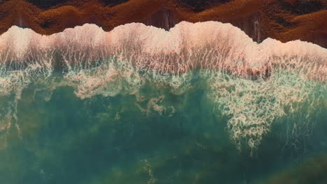 aerial view of ocean waves crashing on a dark sand beach