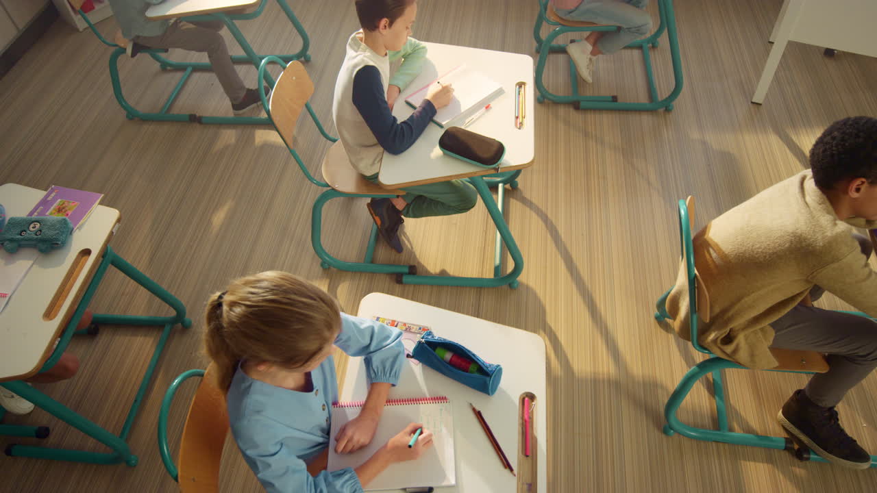 Pupils sitting at desks in classroom. Boys and girl writing in notebooks