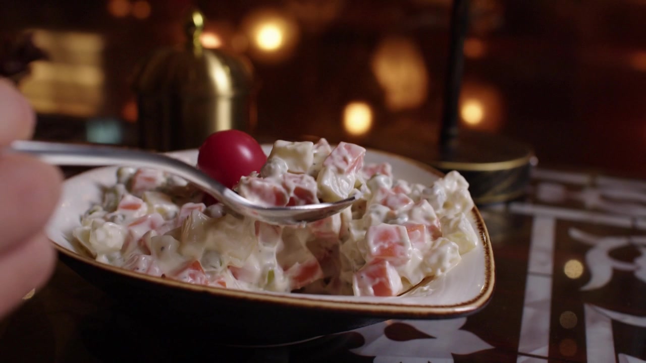 Hand scooping creamy vegetable salad from a decorative bowl on a patterned table