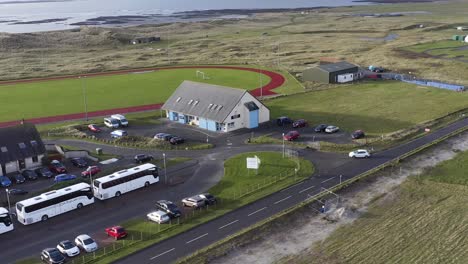 dynamic, drone tracking shot of a car driving through benbecula near the track and football pitch