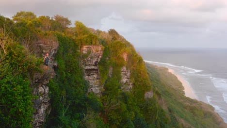 young girl standing on edge of beachside cliff and opening arms to soak in beautiful nature during early morning