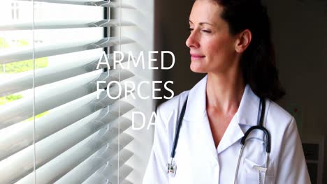 Animation-of-armed-force-day-over-thoughtful-caucasian-female-doctor-standing-at-window