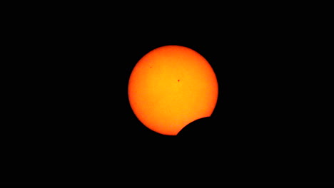 la etapa temprana de un eclipse solar total con la luna comenzando a cubrir el disco solar y dos manchas solares visibles en la superficie del sol