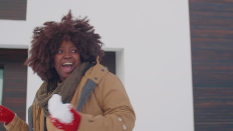 excited african american woman playing snowballs outside