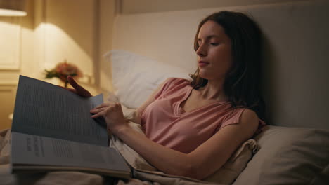 smiling girl reading book in bed evening closeup. relaxed woman resting bedtime