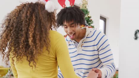 Video-De-Una-Feliz-Pareja-Diversa-Con-Cuernos-De-Reno-Y-Sombrero-De-Papá-Noel-Bailando-Junto-Al-árbol-De-Navidad-En-Casa