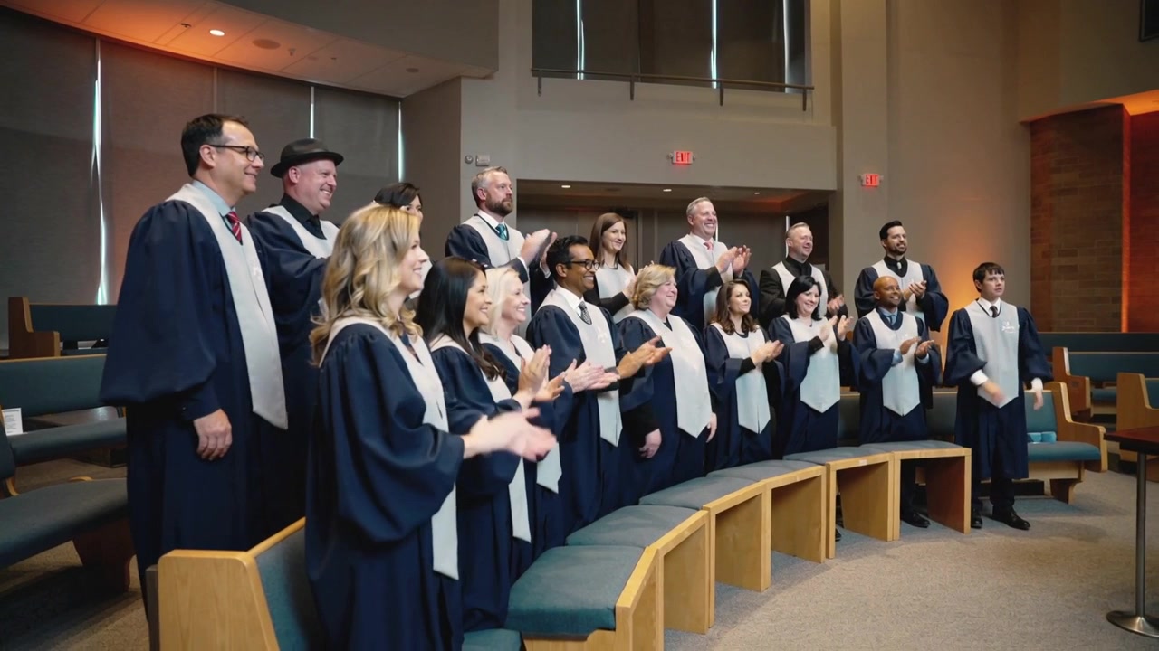 Clapping and singing, choir responding to conductor cue in chapel, navy robes, then lowering hands
