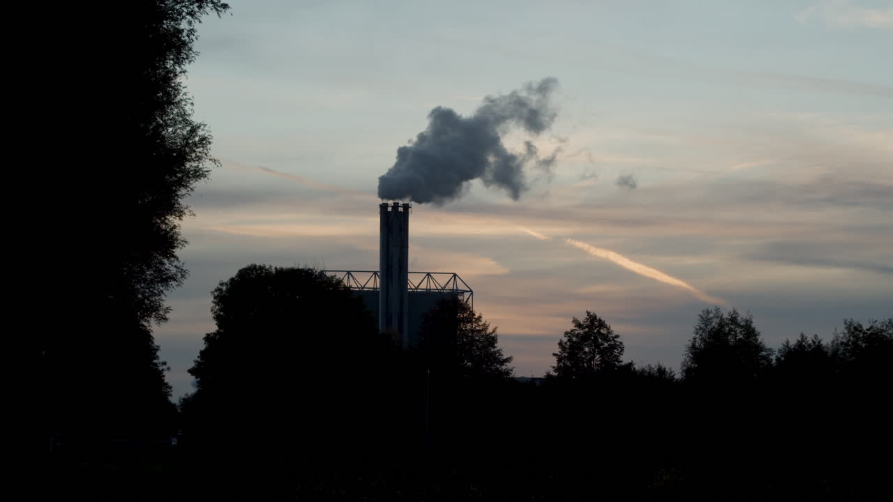 Splendida silhouette di una ciminiera fumante di fabbrica contro un tramonto in tempo reale
