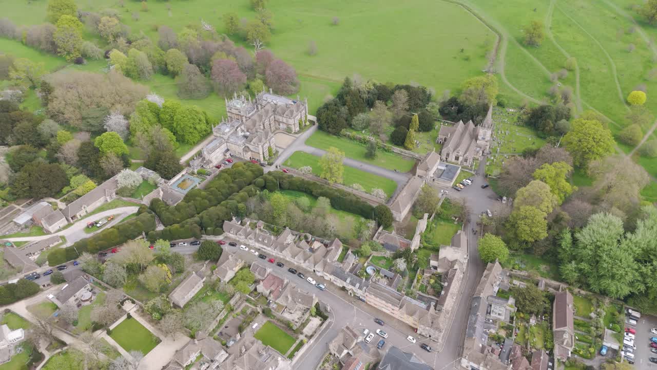 Aerial flyover of stately Corsham Court manor framed by formal lawns, winding gravel paths, sculpted trees and historic stone walls, embodying heritage architecture and landscaped elegance