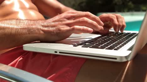 Hombre-Guapo-Usando-Laptop-Junto-A-La-Piscina