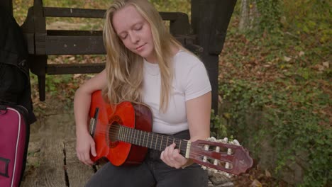 Joyful-Singer-songwriter-female-guitarist-rehearses-by-wishing-well