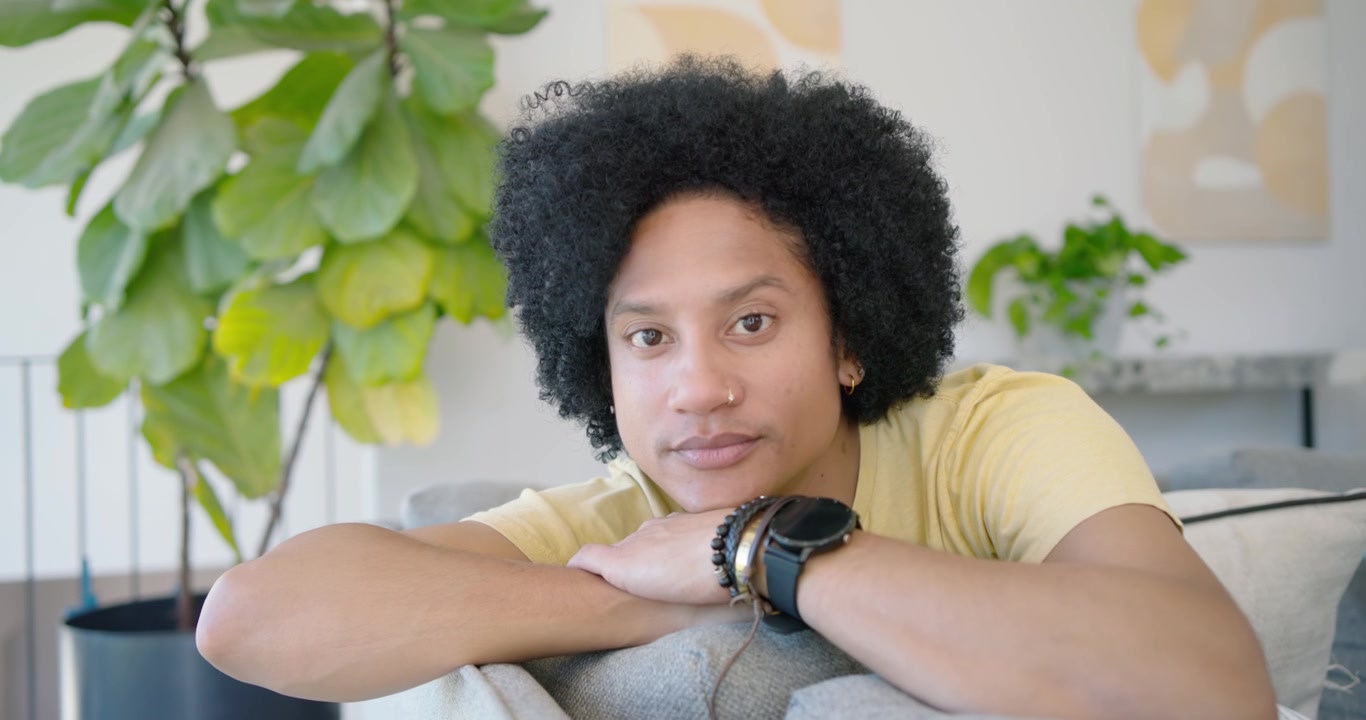 Uomo afroamericano adulto sdraiato sul divano vicino alla finestra con una maglietta gialla, telecamera che si muove con lo sguardo che cambia