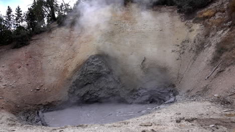 geothermal mud pot boils and steams at base of hill