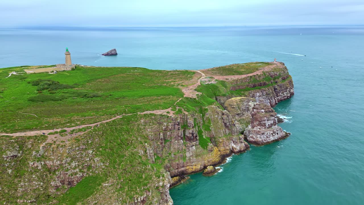 Panoramic drone movement around the Cap Fréhel rocky peninsula and its lighthouse surrounded by beautiful sea waters, Côtes-d'Armor, Brittany, France.