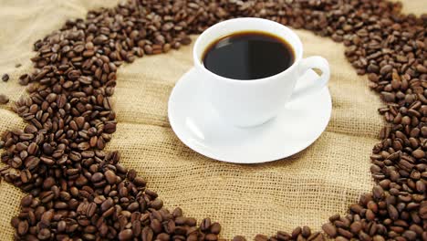 cup of coffee surrounded with roasted beans