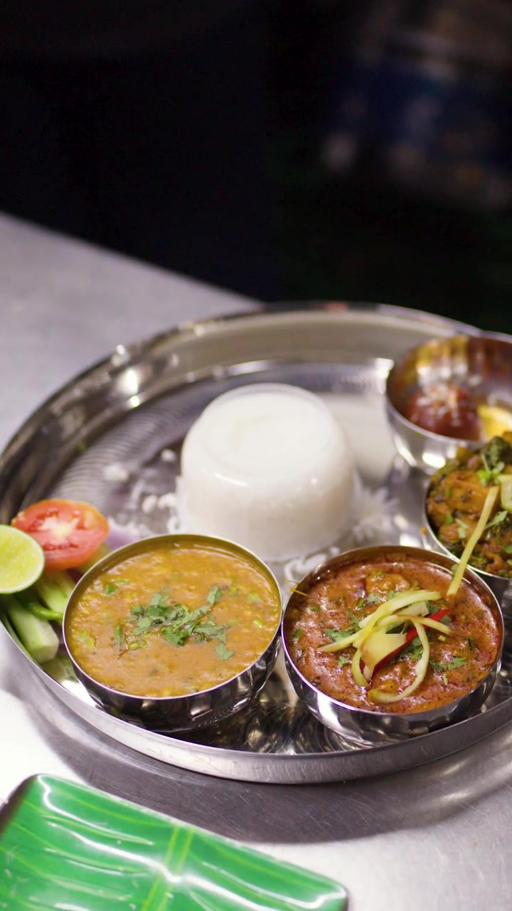 Camera moves slowly over a freshly prepared traditional Indian thali meal in a restaurant kitchen.