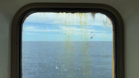 sailboat sailing on calm sea water as seen through dirty and rusty window of navigating old ferry