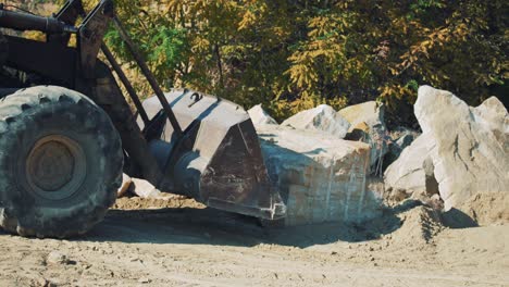 old excavator in a stone quarry with a bucket loads broken stones. sandstone mining