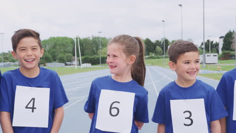 portrait of children on athletics track wearing competitor numbers on sports day