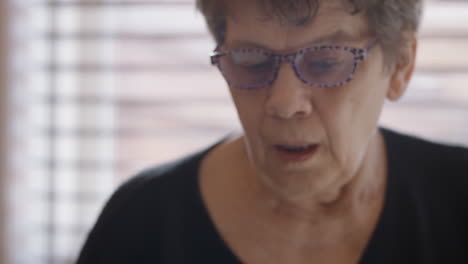 close-up shot of a smartphone resting face-up on a shiny glass top kitchen table beside a vibrant, patterned coffee mug. a woman in a black v-neck top scrolls on phone, as camera tilts up to her face.