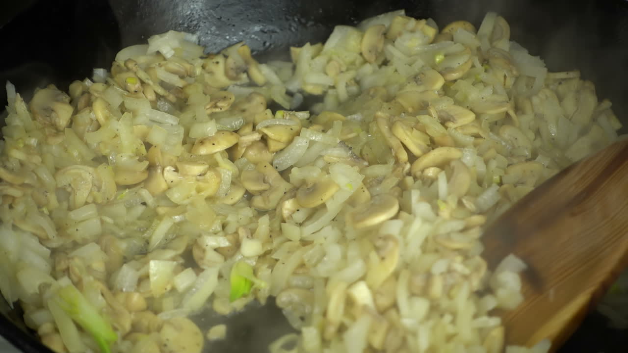 Preparação de cogumelos champignon com cebola. Câmera lenta. Panela de ferro fundido.