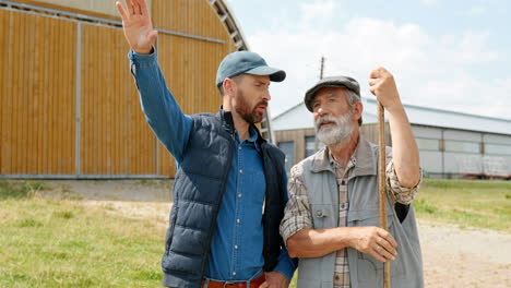 caucasian young man and his senior father talking and walking outside the stable in the field