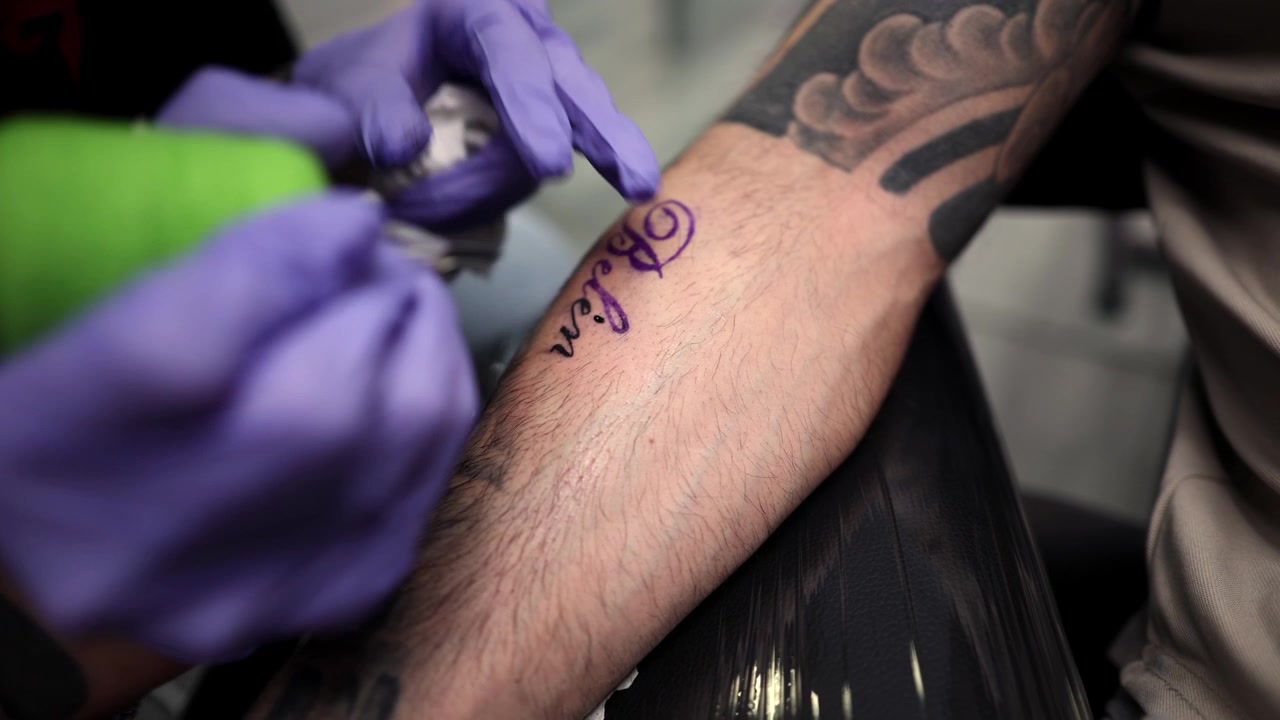Tattoo Artist Inking a Name on a Client's Forearm