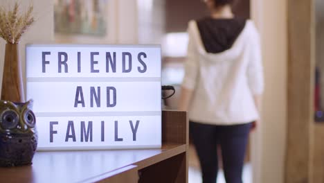 woman walks in and switches on decorative lightbox written friends and family in comfy and cozy home