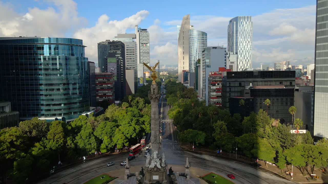 Aerial view descending on Paseo de la Reforma with the Angel of Independence in the foreground, modern buildings on either side on a sunny day in Mexico City