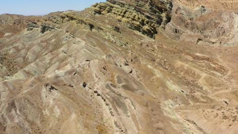 drone view flying over a curving and winding road at the foot of dry mountains and geologic formations in the mojave desert